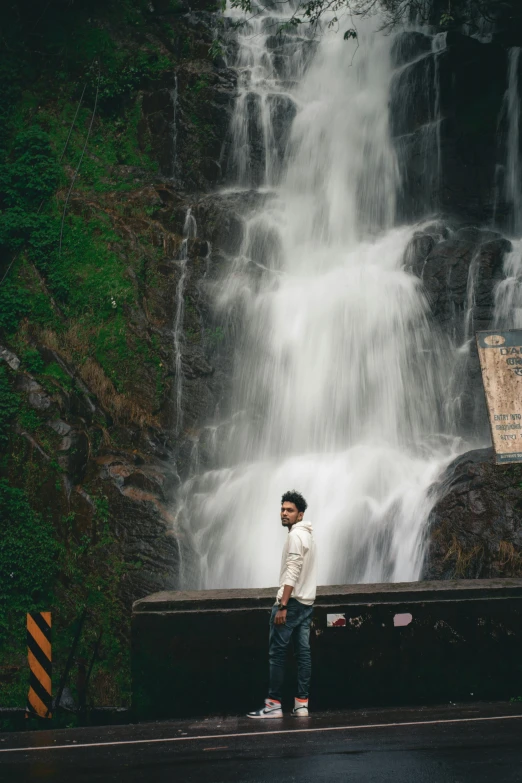 a young man stands in front of a waterfall