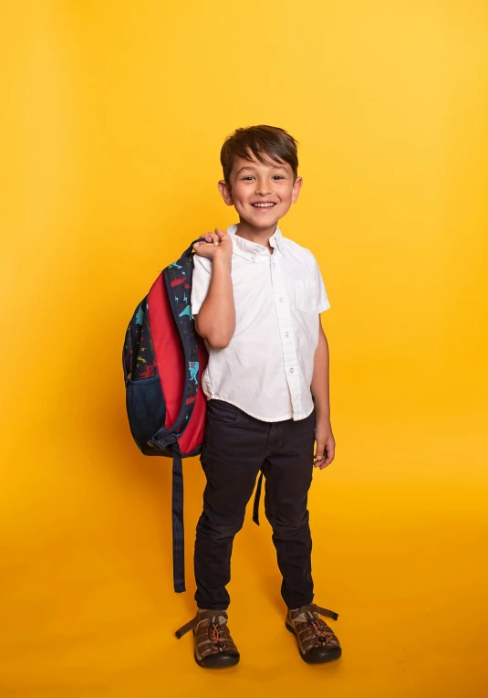 a boy in shirt and pants holding a backpack