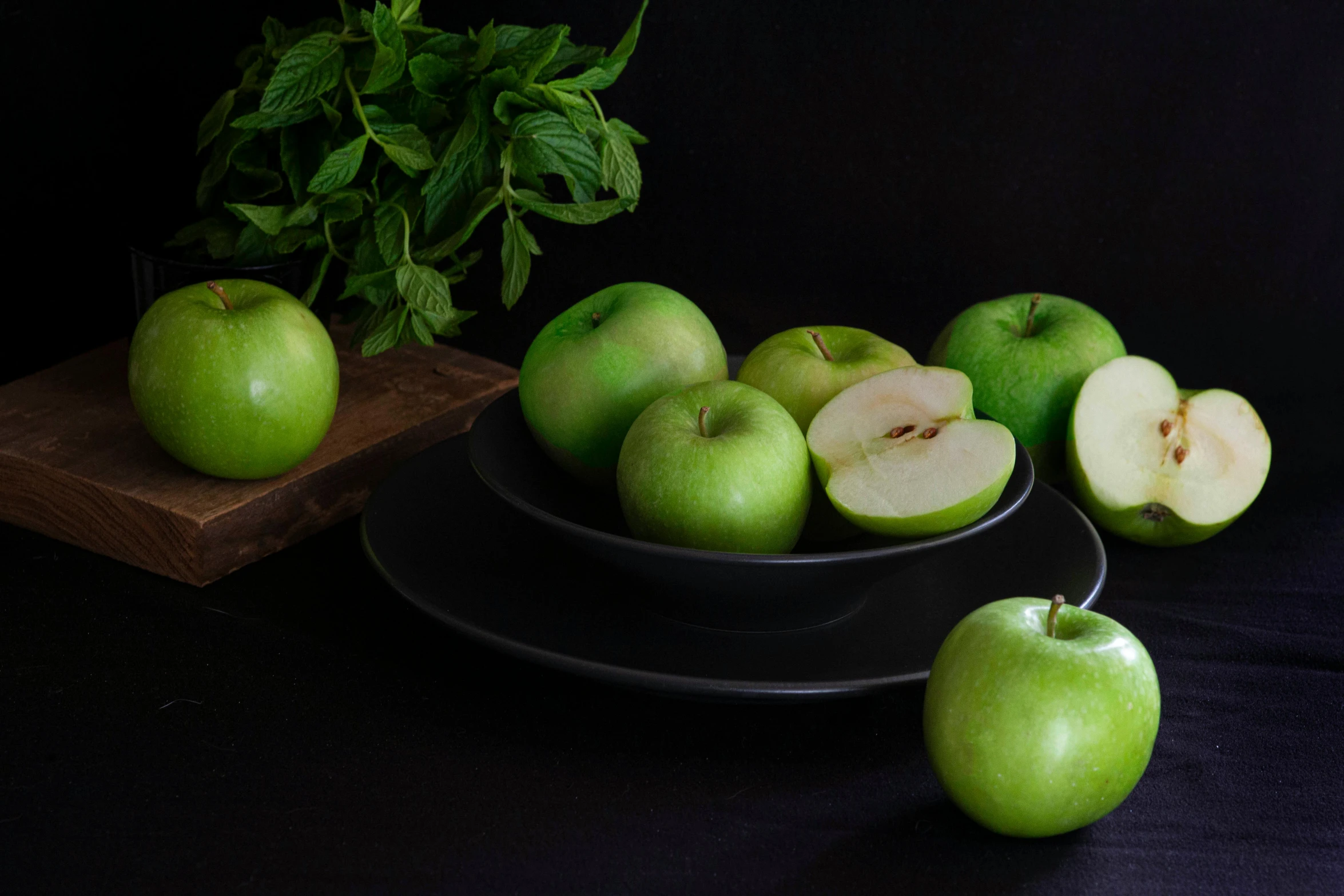 green apples sit next to a bowl of sliced fruit