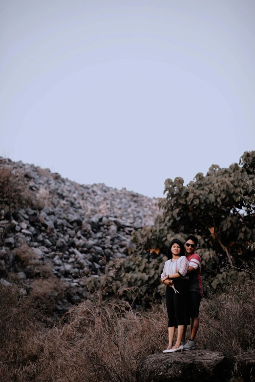 a couple of people standing on top of a rock covered hill