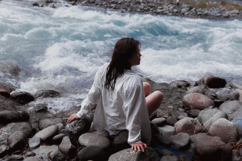 a  sits on a rock near a river