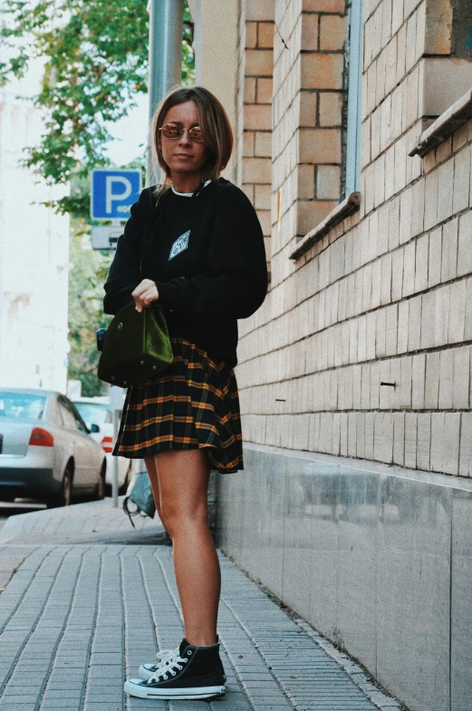 a person in skirt and sneakers is standing on the sidewalk