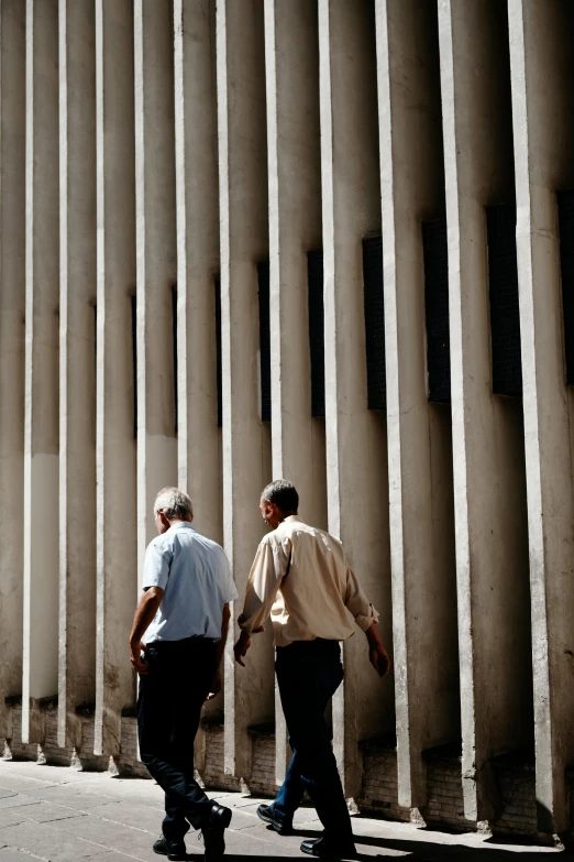 two men walking down the sidewalk by a tall building