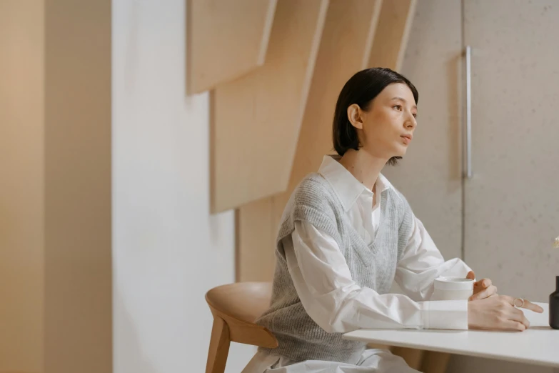 woman sitting at table holding cup looking away from the camera