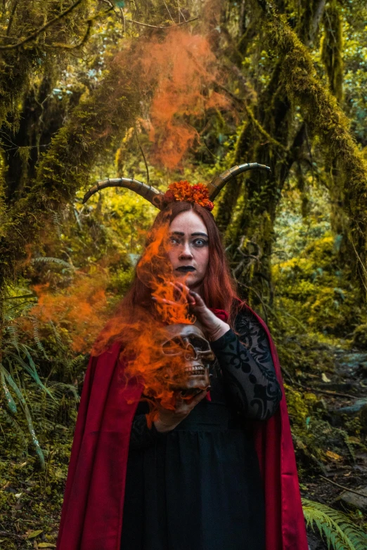 a woman with red hair is dressed in a cloak, surrounded by trees and bushes
