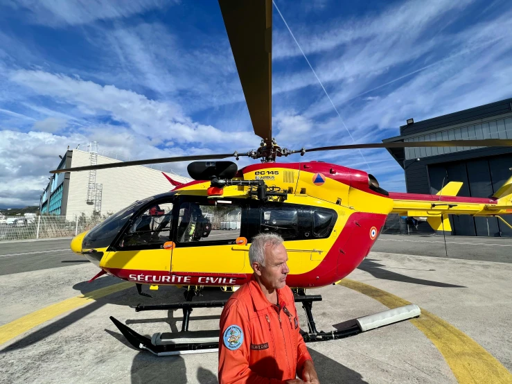 the man is outside in front of a yellow and red helicopter