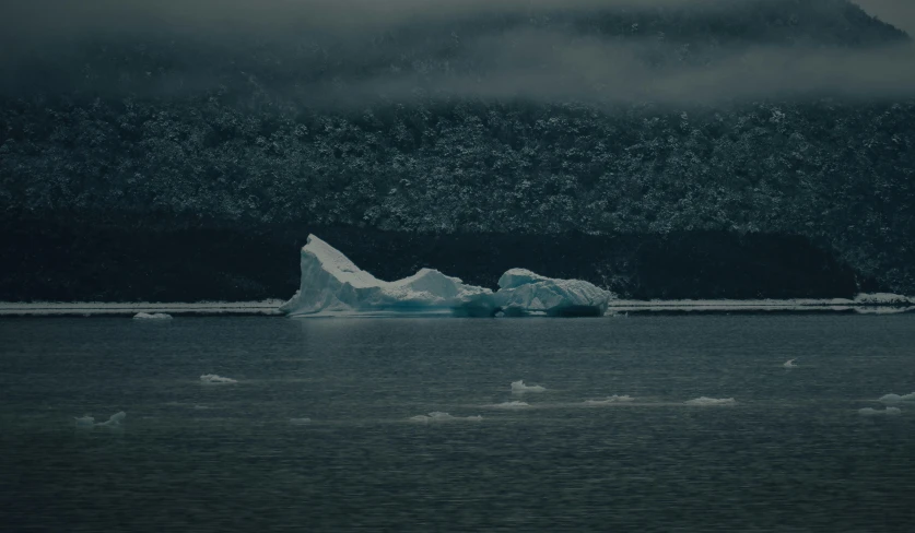 an iceberg floating in the ocean on an overcast day