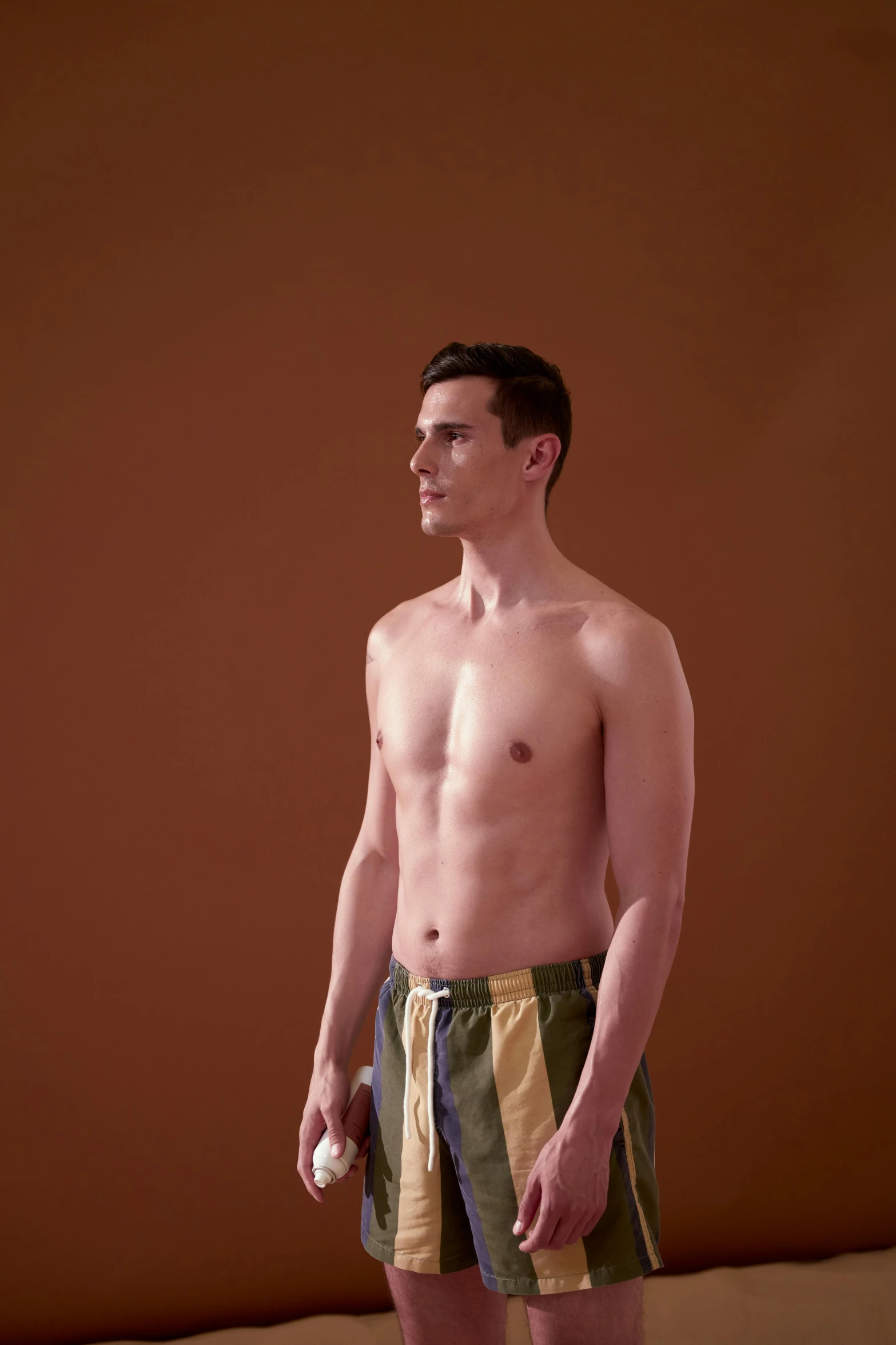 shirtless young man standing in the sand holding a frisbee