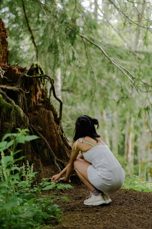 a woman crouches in the woods to look at her watch
