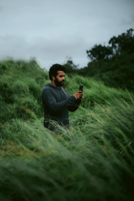 the man is looking at his cell phone while standing in the grass