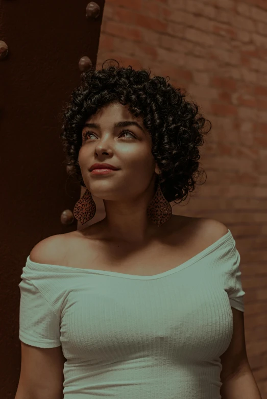 a woman with black curly hair standing in front of a brick wall