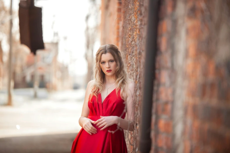 a woman wearing a red dress posing in front of a brick wall