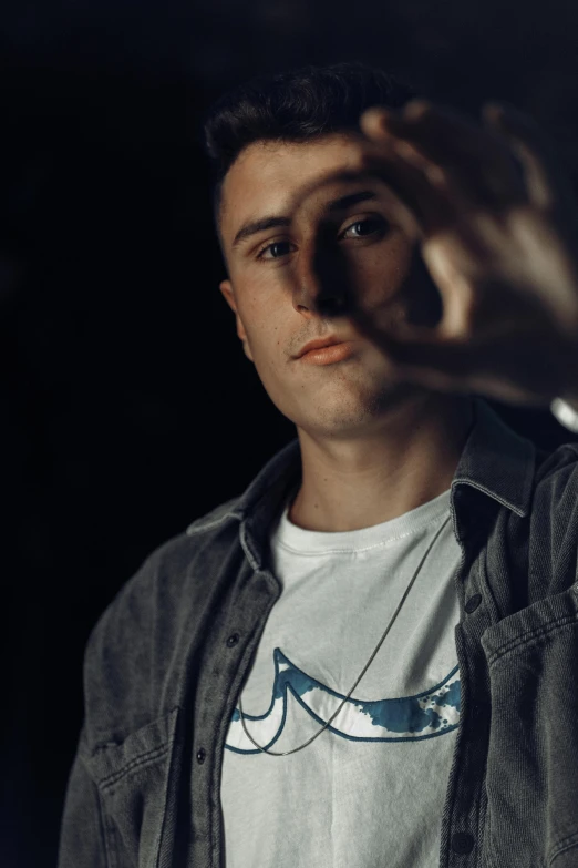 a young man holding a cigarette and wearing a white t - shirt