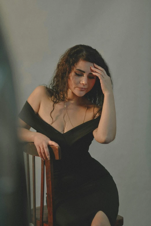 a woman sitting on a wooden chair in a black dress