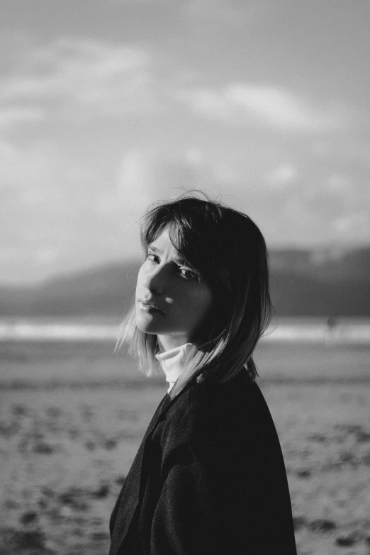 a woman standing on the beach with mountain and clouds in the background