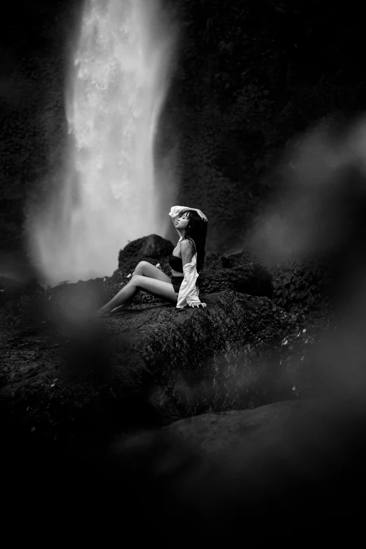 a woman sitting on top of a rock by a waterfall