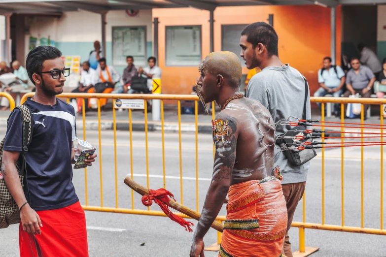 man in red and yellow sarong, standing next to a young man