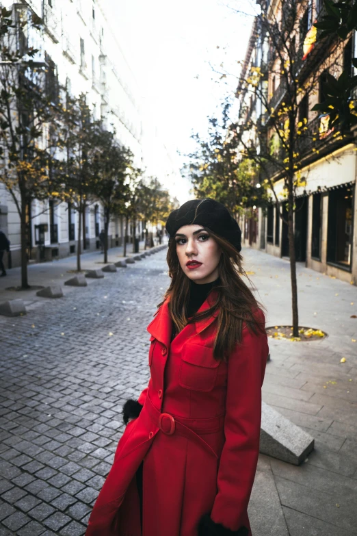 a young woman in red coat and black hat posing on a brick sidewalk