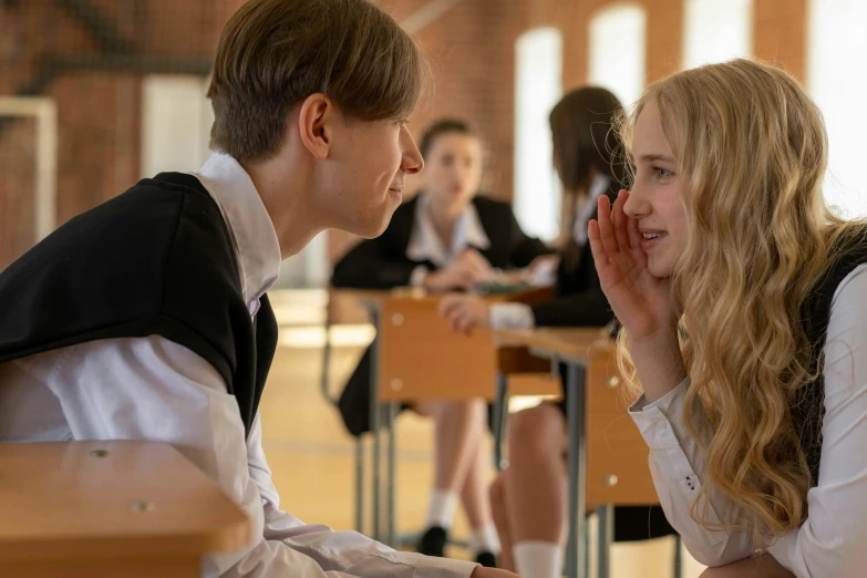 a girl and a boy with hands in their ears are talking in a classroom