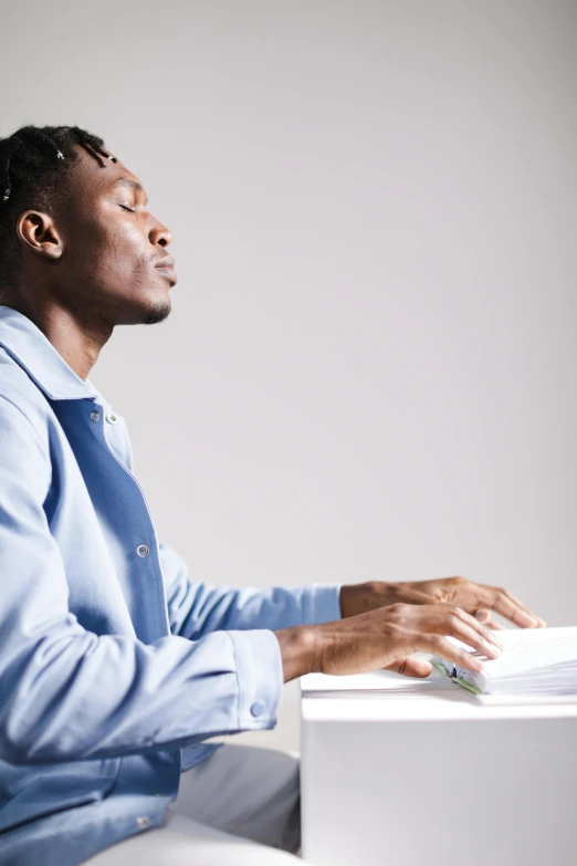 an african american man in a blue shirt sits at a desk with his eyes closed