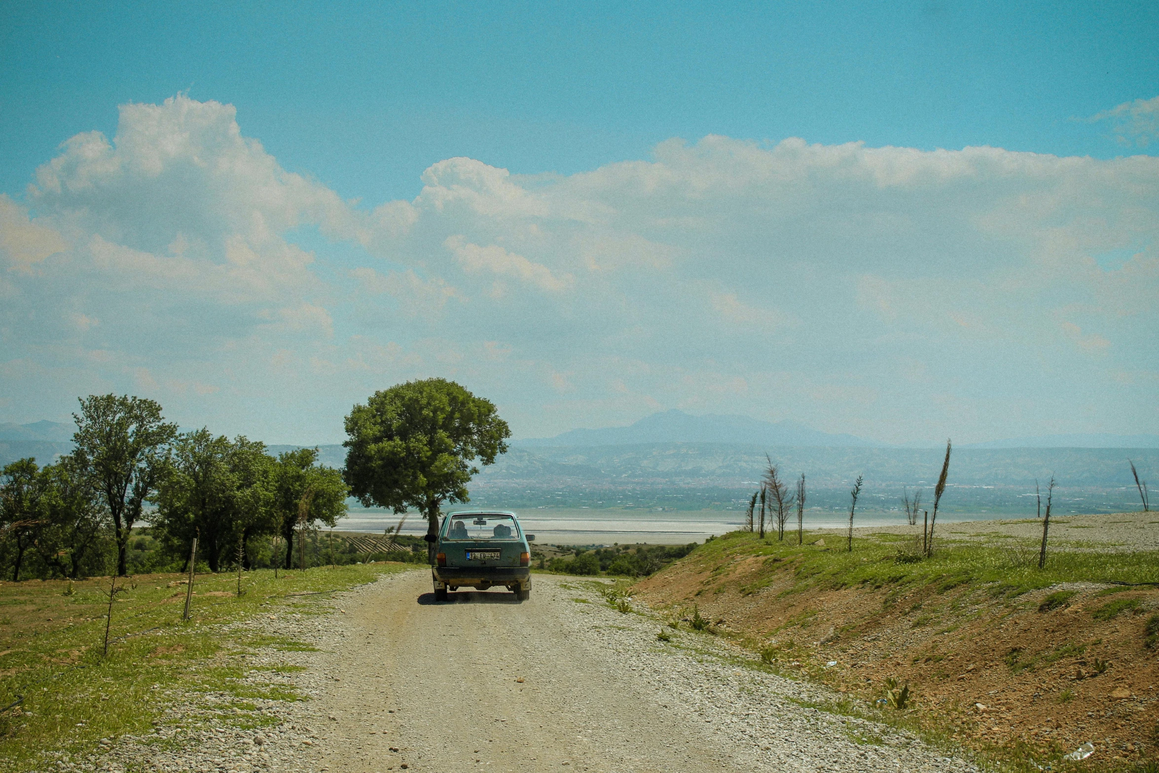 a truck driving down a gravel road next to a green grass covered field