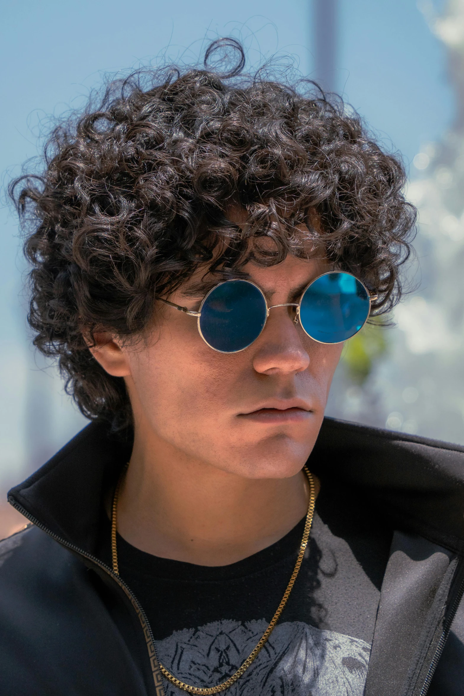 a man with curly hair and round sunglasses looking off to the right