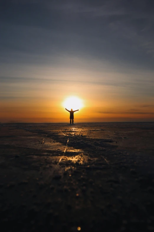 a person stands at the edge of a body of water with their arms up as the sun sets behind him