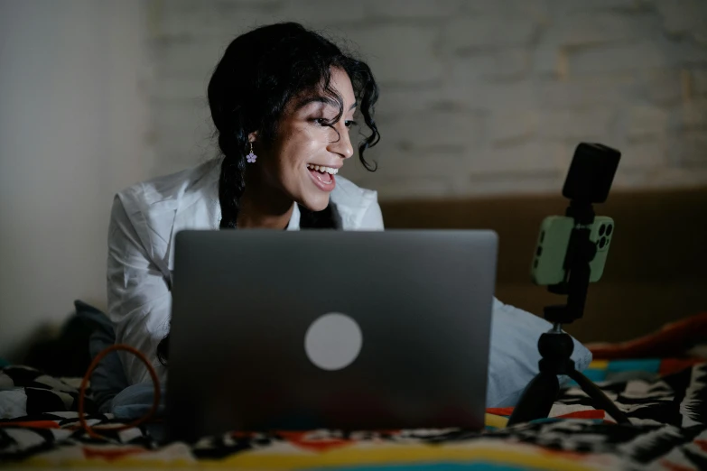 a woman sits on a bed in front of a laptop computer