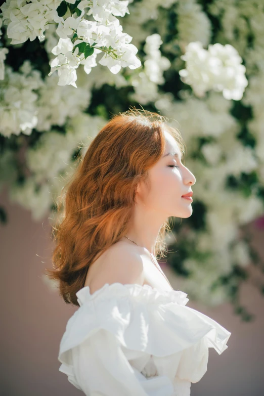 a beautiful young woman is looking up under a large white flower bush