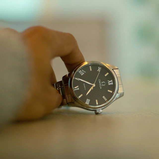 a watch is on the table with a hand near it