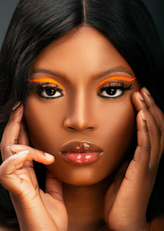 a woman wearing orange eyeliners with her hand on her cheek