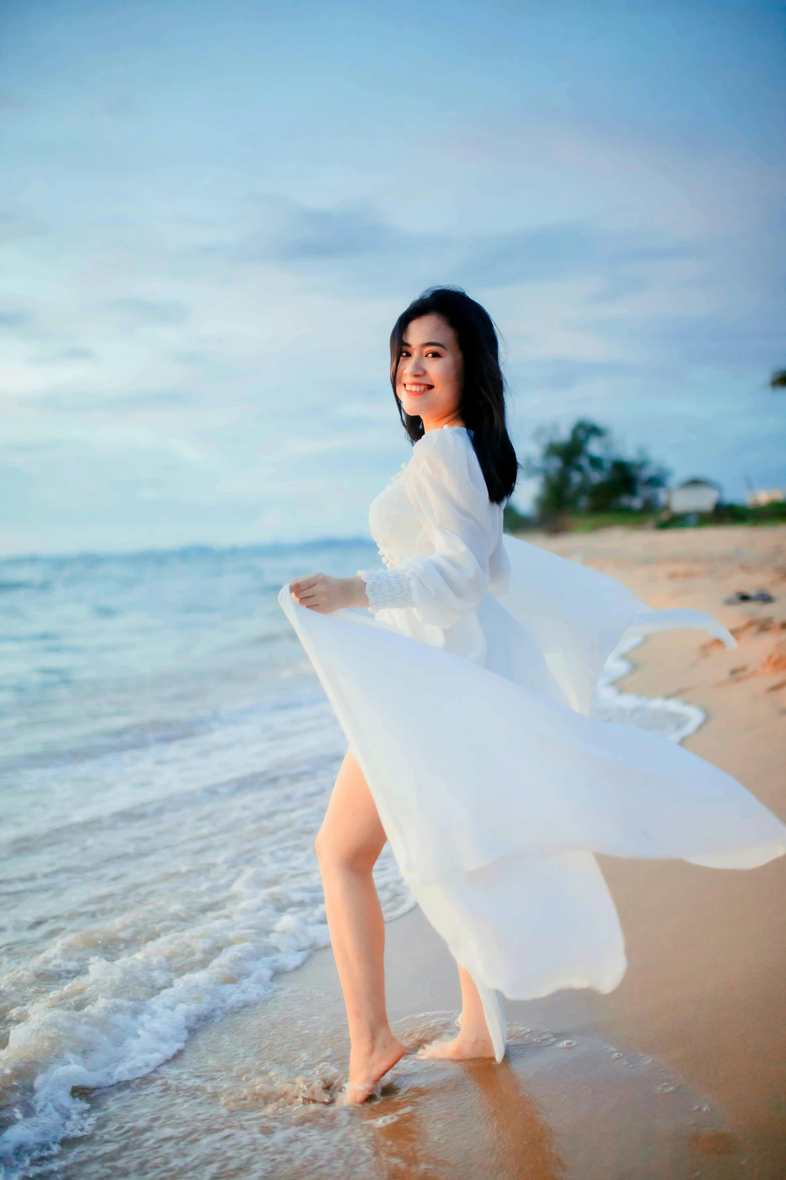 a woman in a long white dress stands on the beach