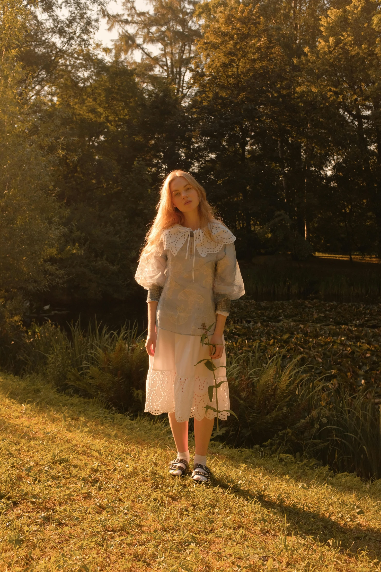 a woman standing in a field near some trees