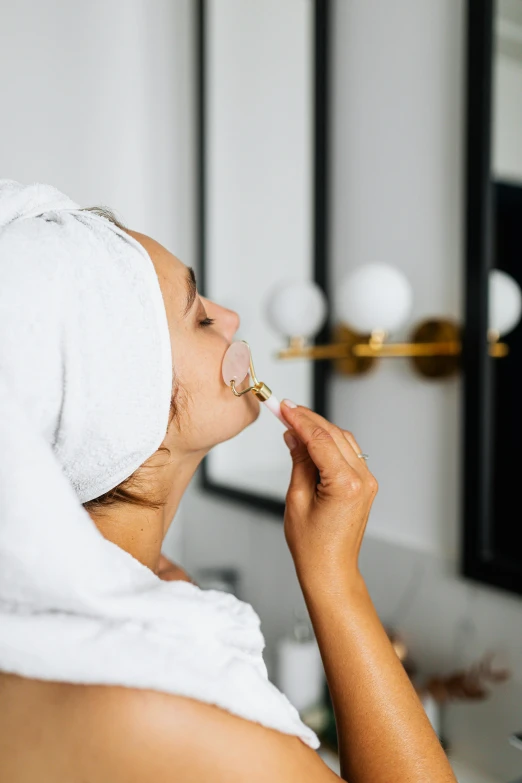 a woman in a towel on her head, putting on a nose ring