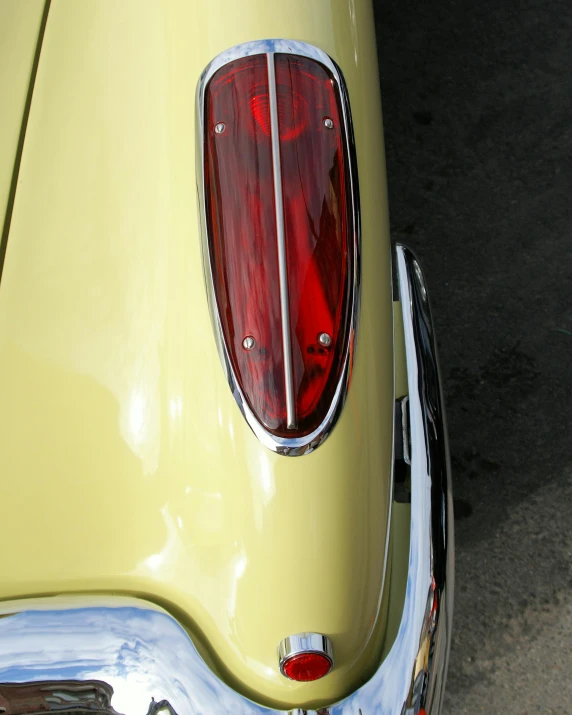 an old yellow car with chrome trim and a rear light