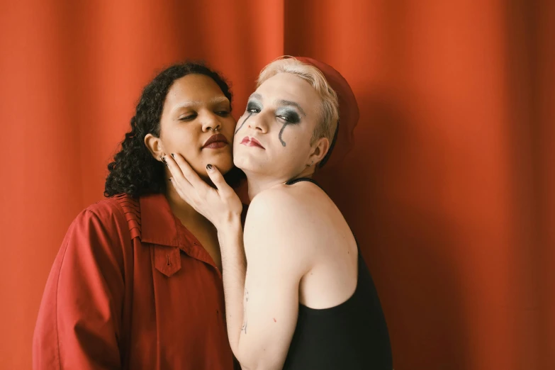 two women with makeup painted, one holding her face behind the other