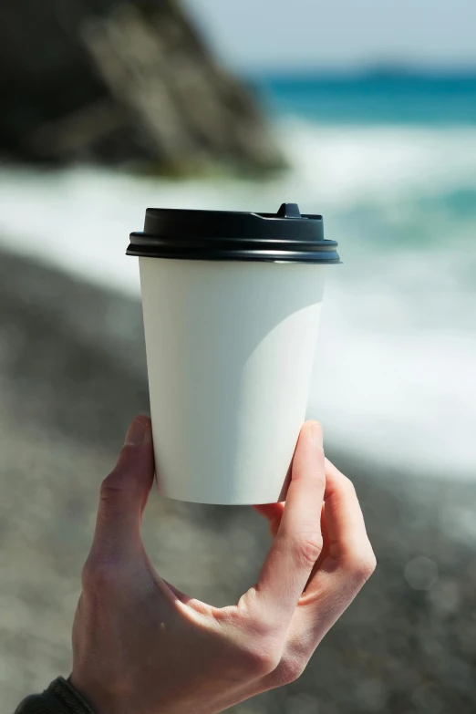a person holding up a cup with the ocean in the background