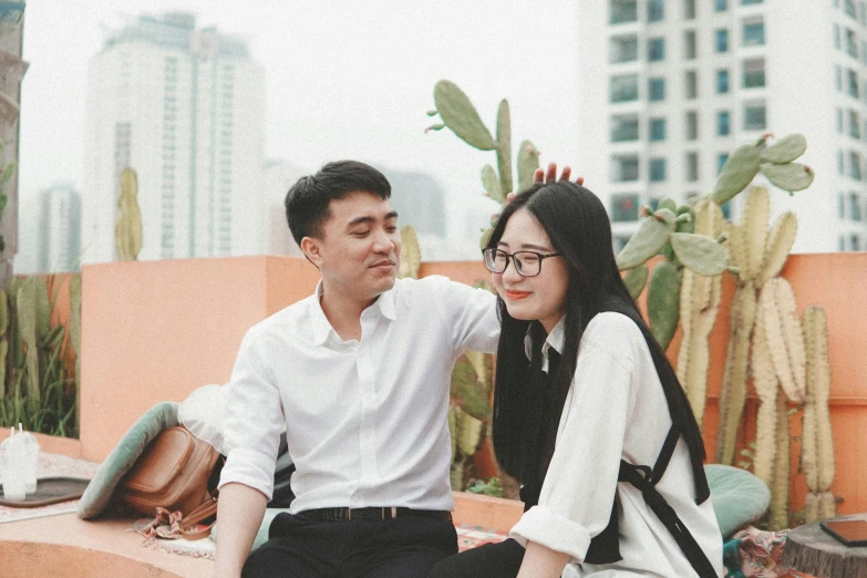 a man and woman sitting on the edge of a roof with cactus in the background