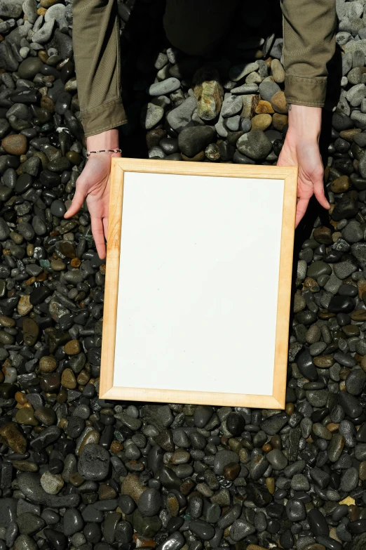 person's hands holding a picture frame on some rocks