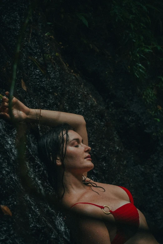 woman in a red bikini is posing on the edge of a waterfall