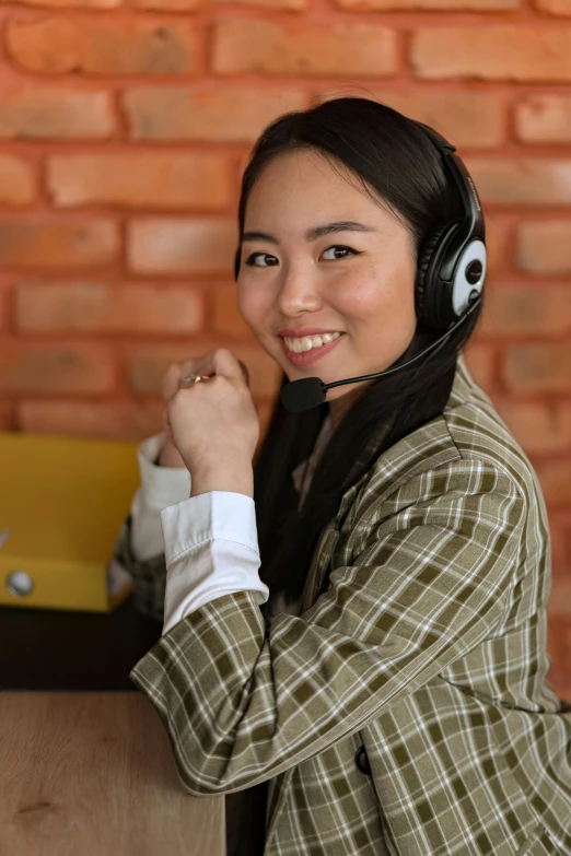 woman with headphones smiling in front of red brick wall