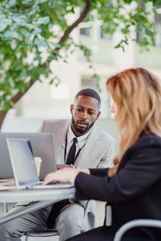 a man sitting in front of a woman using a laptop computer