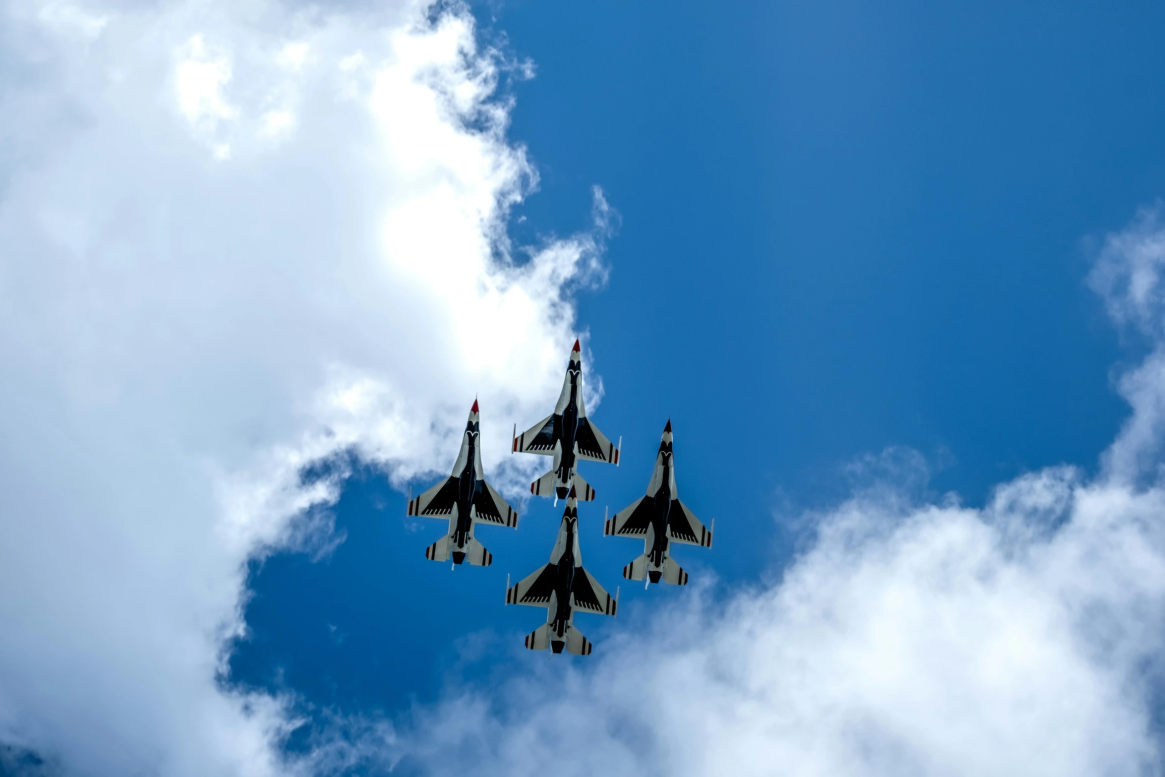 four fighter jets in formation with the clouds behind them