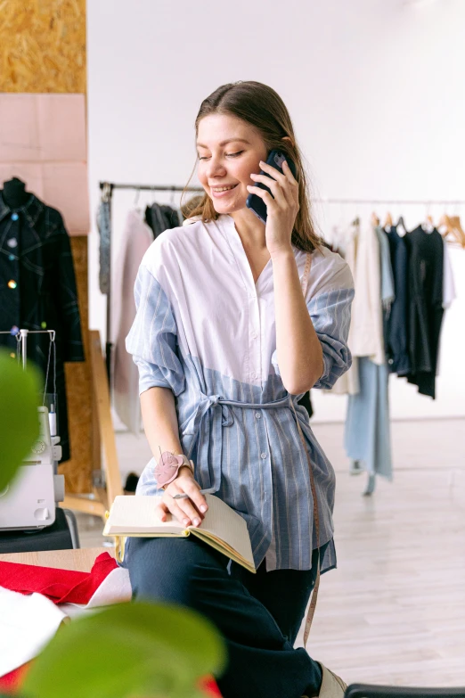 a woman sitting on the ground holding a book while talking on a cell phone