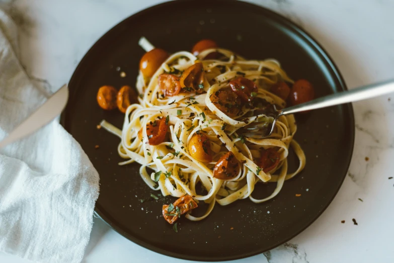 a black plate with spaghetti and tomatoes on it