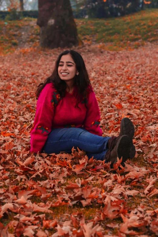 a woman smiles while sitting in leaves in a park