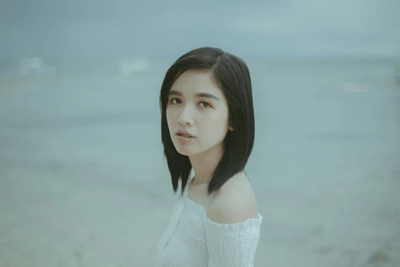 a woman with long black hair standing on a beach