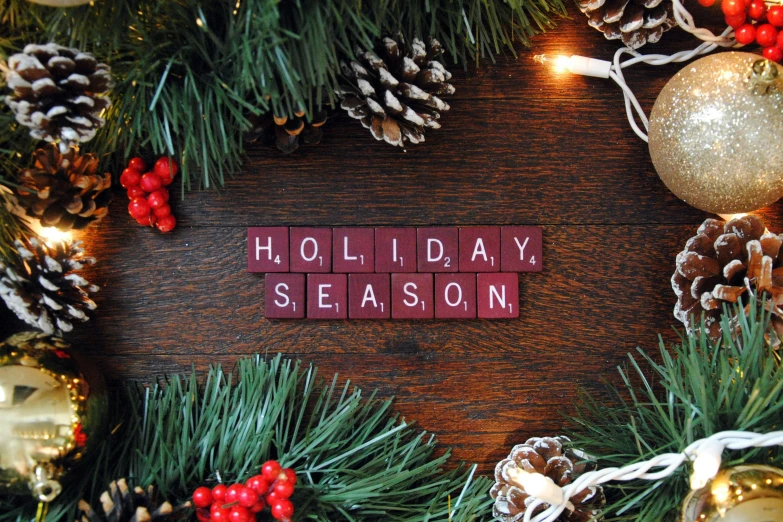 the word holiday season written on tile surrounded by pine and christmas decorations