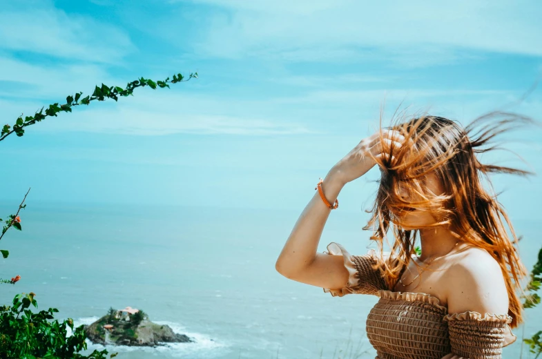 a woman is standing next to the ocean and waving her hair