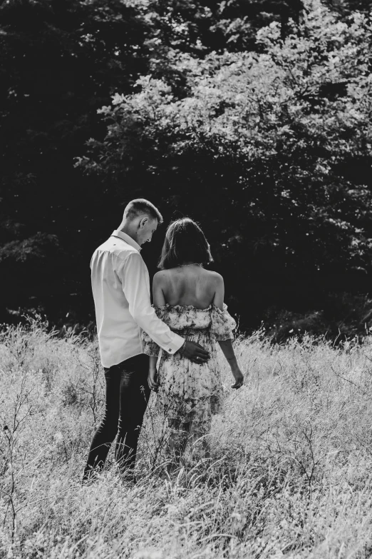 a man and woman holding each other walking through tall grass